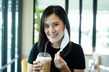 Asyalı güzel bir kadın mavi bir maske çıkarmalı ve sabah mutlulukla buzlu kapuçino içmeli..