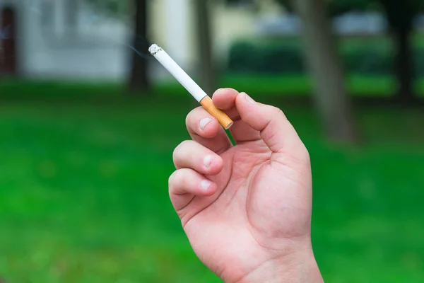 Cigarrillo en la mano con humo sobre fondo verde — Foto de Stock