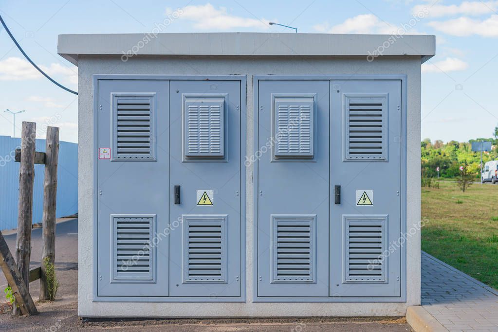 Electric Transformer room  building with grey doors and yellow hazard signs on blue sky background