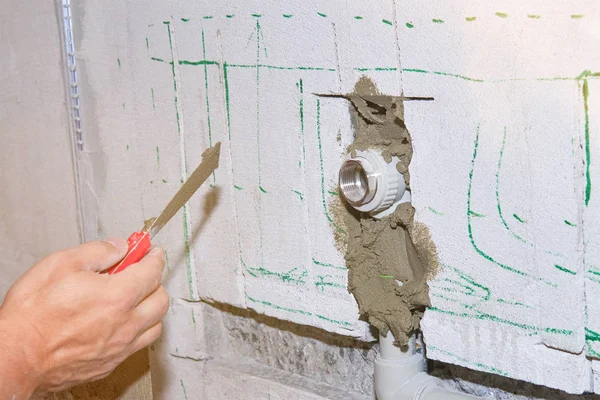 Строитель держит шпатель в руке и покрыт цементным раствором с трубой в стене — стоковое фото