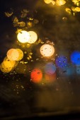 Zaměřit se na popředí. Dešťové kapky na okno auta. Dopravní a městské světla na pozadí.