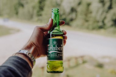 Lubana, Letonya. 1 Ağustos 2019. Adamın biri elinde bir şişe Carlsberg Alcochol bedava organik bira tutuyor. Film filtresine benziyor..