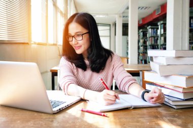 Not alan ve terazi okurken dizüstü bilgisayar kullanan genç bir kadın.