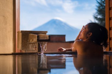 Güzel bir kadın sabahları Japonya 'daki Fuji Dağı' nın manzarasını izleyerek onsen 'in (mineral sıcak banyosu) tadını çıkarır. 