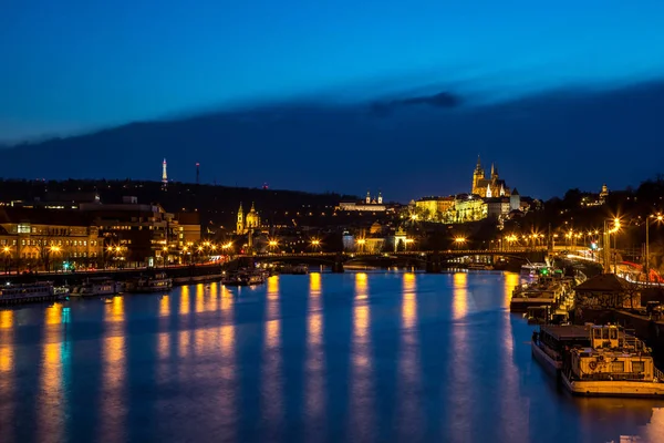 Reflections of the lights on the surface of the river Vltava, night panorama of Prague with bridges and docked boats