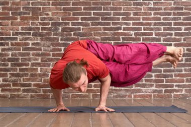 Pratik yoga longhair adam sakallı. Modeli ile kırmızı tuğla duvar odadaki mavi mat egzersizleri yapıyor. Dag Pada Koundinyasana poz. Tam boy