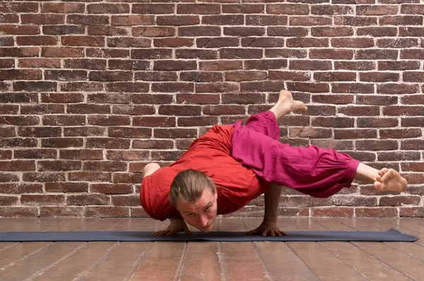 Pratik yoga longhair adam sakallı. Modeli ile kırmızı tuğla duvar odadaki mavi mat egzersizleri yapıyor. EKA Pada Koundinyasana poz. Tam boy