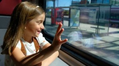 Kız trenle seyahat eder ve pencereden bakar, elini sallar..