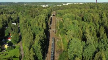 Yüksek hızlı banliyö treninin hava görüntüsü Finlandiya 'nın Espoo kentindeki kırsal kesimde demiryolunda ilerliyor. Tepeler arasındaki demiryolu bir tünele gidiyor..