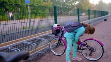 Kız okul bisikletinin park yerine bir bisiklet asmaya çalışıyor..