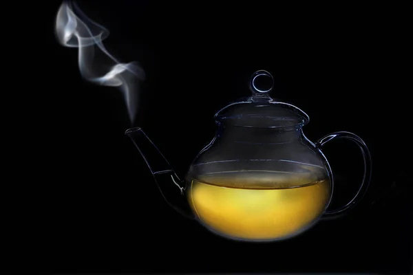 one object on a black background, a glass transparent teapot with tea, steam comes out of the spout