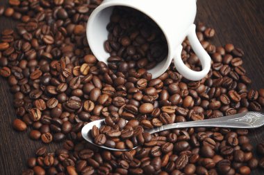 kahve çekirdekleri toplu ahşap arka plan üzerinde. Üzerine beyaz bir bardak ve kaşık ise