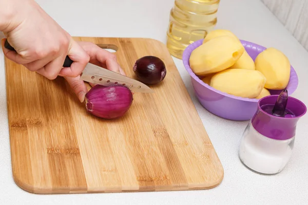 cutting onions on a cutting Board with a knife. standing next to the bowl of potatoes, oil and salt