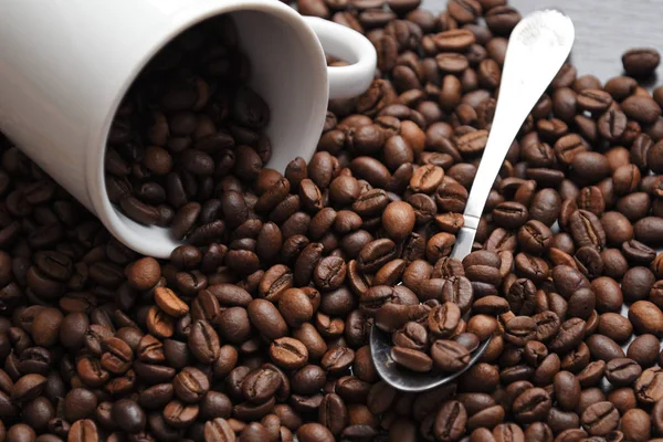 kahve çekirdekleri beyaz bir bardaktan dökülür. fasulye yanındaki bir kaşık olduğunu