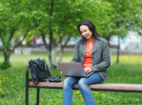 Dizüstü bilgisayarda çalışan genç freelancer kız, parkta bankta oturuyor