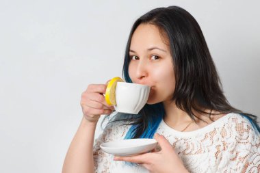 Bir kız bir limonlu çay içiyor. Tatlı bir içki. Nötr arka plan. Önden görünüm. Yakın çekim.