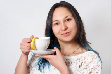 Bir kız bir limonlu çay içiyor. Tatlı bir içki. Nötr arka plan. Önden görünüm. Yakın çekim.