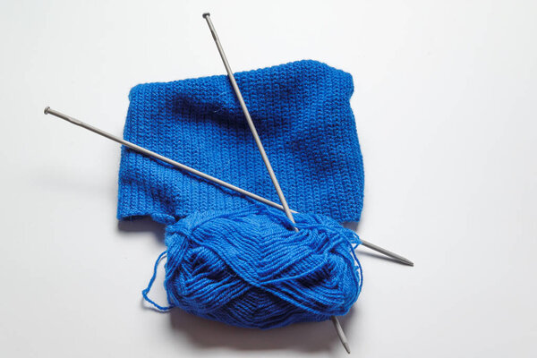клубок синей пряжи с двумя спицами, нанизанными на заднем плане. вязание, рукоделие, собственные руки
