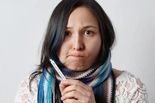sad girl with a cold disease in a scarf holding a medical thermometer