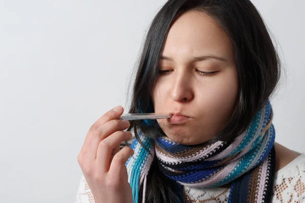 sad girl with a cold disease in a scarf holds a medical thermometer in her mouth