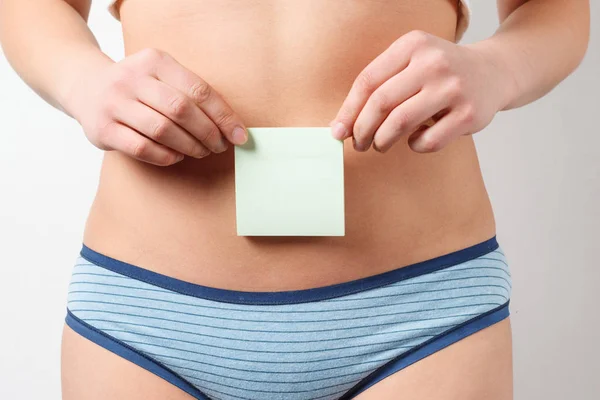 灰色の背景に 葉書を保持している女性の腹のクローズ アップ 女性の健康 婦人科 期待の概念 — ストック写真
