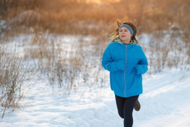 Mavi bir ceket ve çalışan spor kadın. Kışın açık havada karda koşu