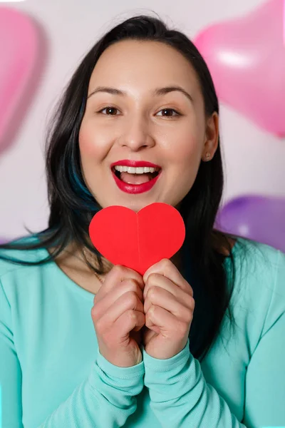 Valentine's Day. Beautiful young woman with heart in her hands. Young woman with red heart on white background with inflatable balls. portrait of attractive smiling woman on white studio shot with hearts. close up