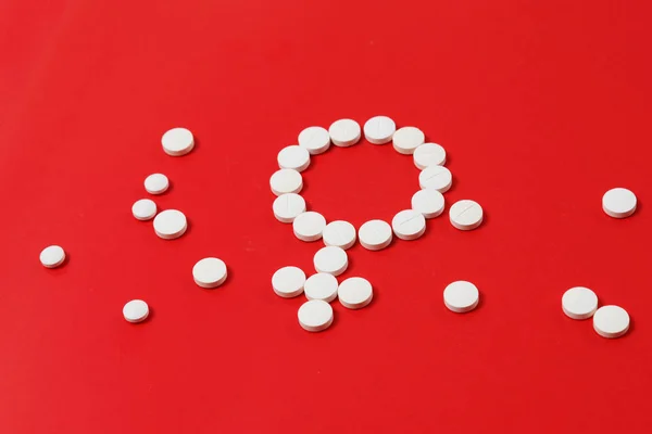 Concept Female health. Gender symbol made from white pills or tablets on red background.