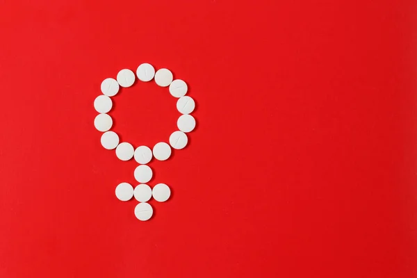 Concept Female health. Gender symbol made from white pills or tablets on red background.