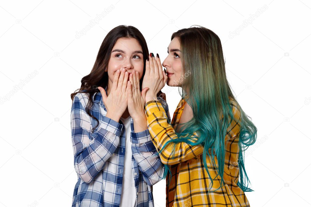 Two female friends gossiping. One girl tells the secrets of the other in her ear. Isolated on white background.