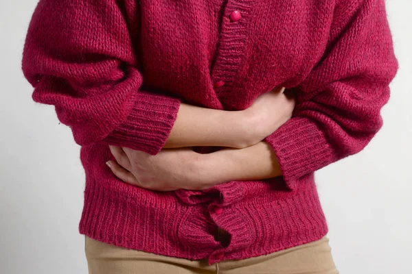 portre fotoğraf. bir kadının midesinde bir ağrı vardır ve onun ellerini tutar. Kadın tıp kavramı. Sindirim sorunları, kadın hastalıkları gebelik, adet kanamaları, mide