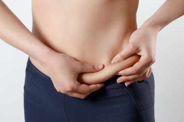 genç bir kadın iki eli karnında kıvrımlar hissediyor. Işık beyaz arka plan üzerinde. Kilo kaybı, doğru beslenme, aşırı kilo, kadın sağlığı kavramı