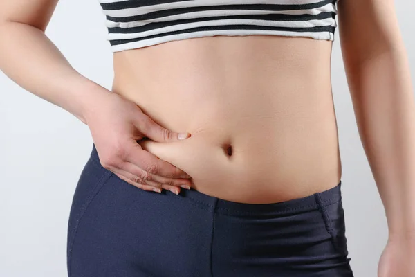 Young woman feels hand folds on her stomach. On light background. Concept of weight loss, proper nutrition, excess weight, women's health and — Stock Photo, Image