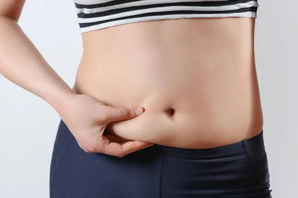Ung kvinna känns hand veck på magen. På ljus bakgrund. Begreppet rätt kost, övervikt, viktminskning, kvinnors hälsa och — Stockfoto