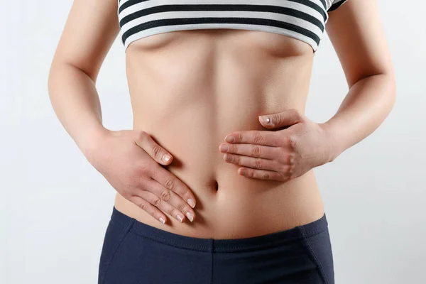 erken gebelik, doğru beslenme, kadın sağlığı kavramı. ince güzel göbek ve göbek bir kadının yakın çekim fotoğraf. Beline ellerini iki avuç dokunur. Beyaz backgr