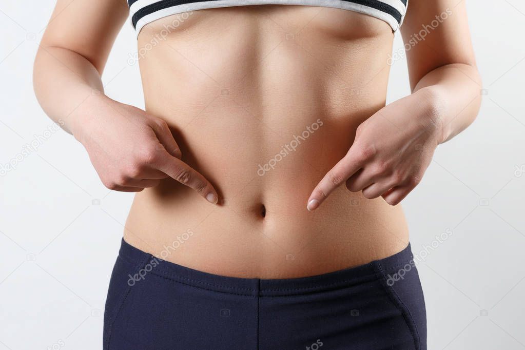 slender beautiful waist of a young woman close-up. on white background. She points two fingers at the bottom of her stomach.