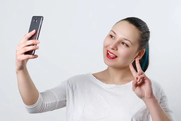 Портрет молодой привлекательной женщины, делающей селфи на смартфоне на белом — стоковое фото