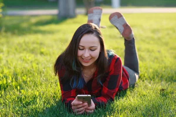 Yeşil çim üzerinde yalan ve açık havada smartphone kullanarak gülümseyen bir kadın portresi