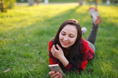 Yeşil çim üzerinde yalan ve açık havada smartphone kullanarak gülümseyen bir kadın portresi
