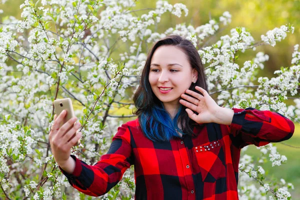 Портрет красивой молодой женщины селфи в парке со смартфоном делает V знак — стоковое фото