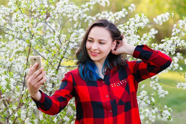 Портрет красивой молодой женщины селфи в парке со смартфоном делает V знак — стоковое фото