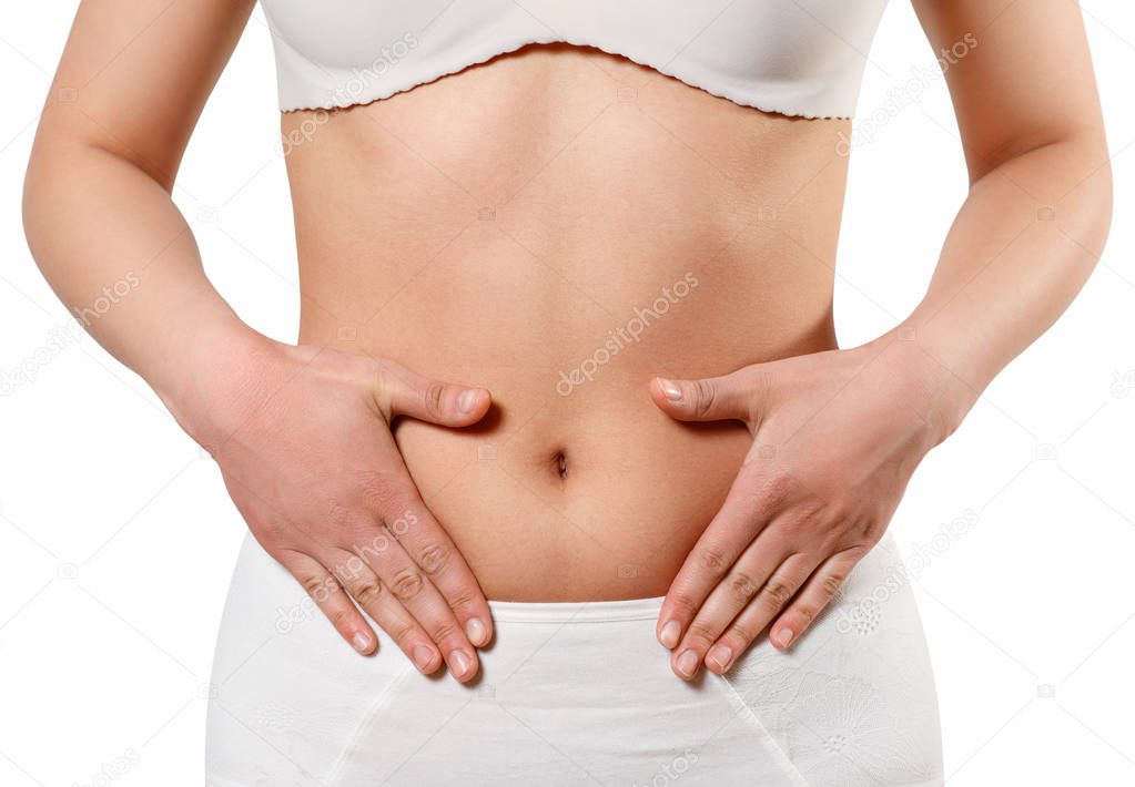 Concept of early term of pregnancy. Close up photo of woman's abdomen and belly button, she is touching her slim stomach with two hands isolated on white background