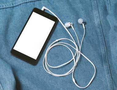 siyah kasa ve boş beyaz ekranlı akıllı telefon ve denim arka planda kulaklık kulak tomurcukları takılı