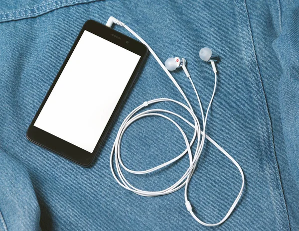 Smartphone com caixa preta e uma tela branca em branco e conectado auscultadores auriculares no fundo da ganga — Fotografia de Stock