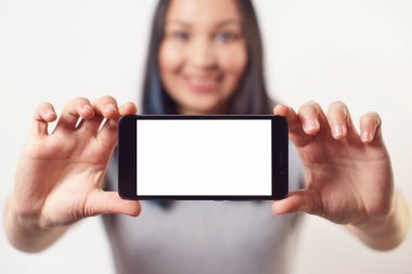 İki eliyle boş beyaz ekranlı bir akıllı telefon tutan ve beyaz arka planda gülümseyen güzel bir kadın