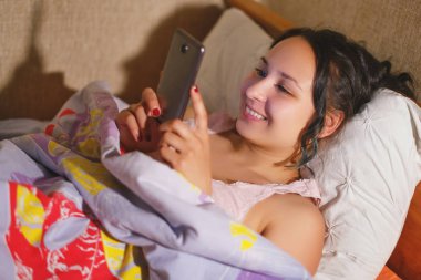 mutlu gülümseyen genç kadın gece evde yatak odasında yatakta akıllı telefon mesajlaşma