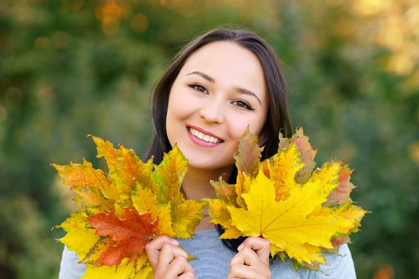 Портрет усміхненої молодої жінки з осіннім листям перед листям — стокове фото