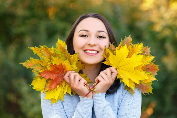 Портрет усміхненої молодої жінки з осіннім листям перед листям — стокове фото