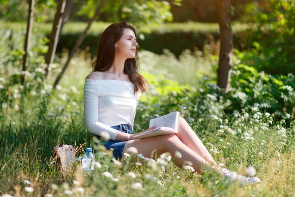 美丽的小女孩在室外的一个夏季公园里看书 — 图库照片