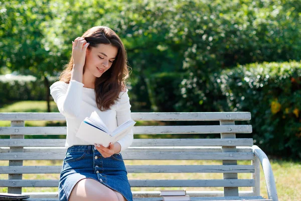 夏天的一天 年轻的女人在公园的长椅上看书 — 图库照片